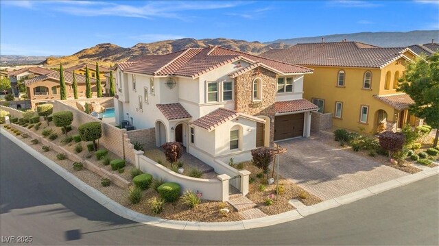view of front of house with a tiled roof, a mountain view, an attached garage, stucco siding, and fence private yard