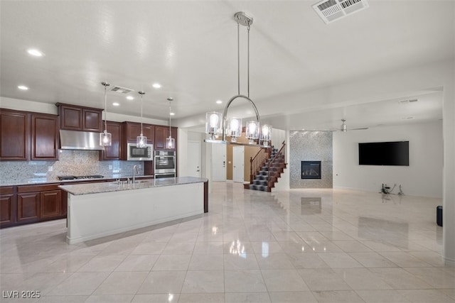 kitchen with under cabinet range hood, visible vents, backsplash, appliances with stainless steel finishes, and a large fireplace