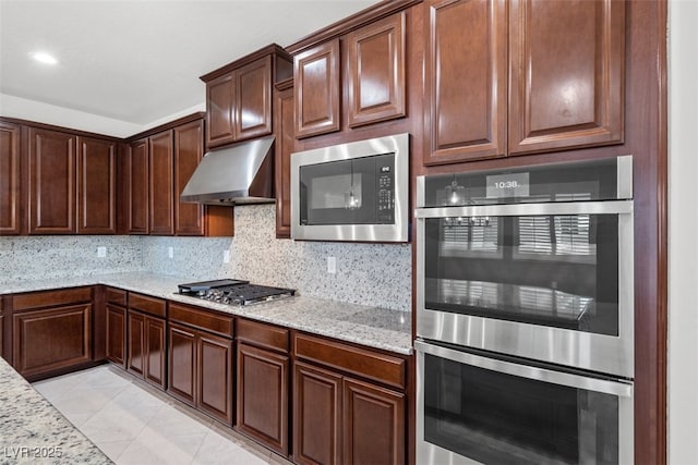 kitchen featuring tasteful backsplash, light stone counters, under cabinet range hood, light tile patterned floors, and appliances with stainless steel finishes