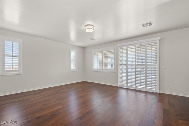 empty room featuring baseboards, dark wood-style flooring, and visible vents