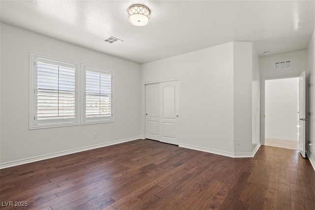 unfurnished room with baseboards, dark wood-style flooring, and visible vents