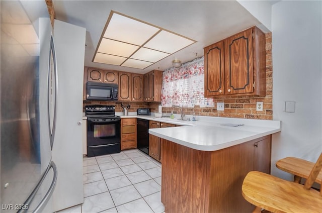 kitchen featuring a peninsula, light countertops, brown cabinetry, and black appliances
