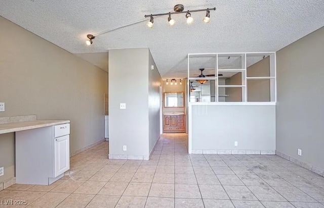 interior space featuring a textured ceiling, baseboards, a ceiling fan, and light tile patterned floors