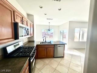 kitchen with a sink, a peninsula, brown cabinetry, dark countertops, and appliances with stainless steel finishes