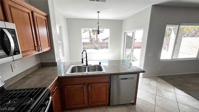 kitchen with a peninsula, a sink, brown cabinetry, a notable chandelier, and appliances with stainless steel finishes