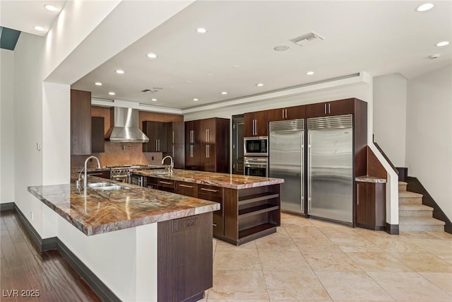9501 Balatta Canyon Ct, Las Vegas, NV 89144 - kitchen featuring built in appliances, a sink, a peninsula, dark stone countertops, and wall chimney exhaust hood