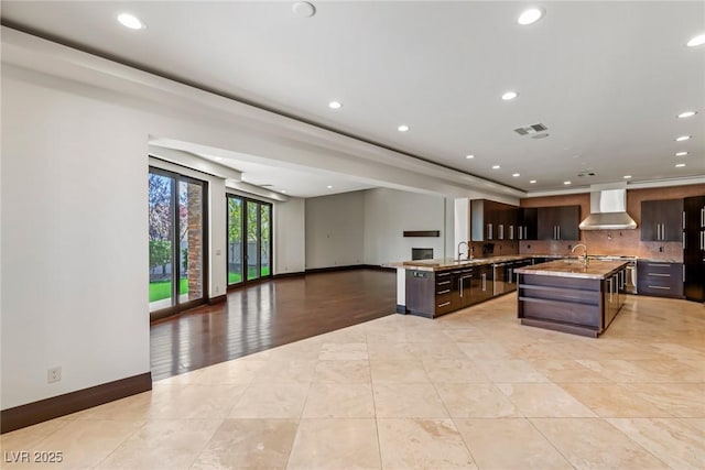 9501 Balatta Canyon Ct, Las Vegas, NV 89144 - kitchen featuring wall chimney exhaust hood, dark brown cabinetry, open floor plan, recessed lighting, and a kitchen island with sink