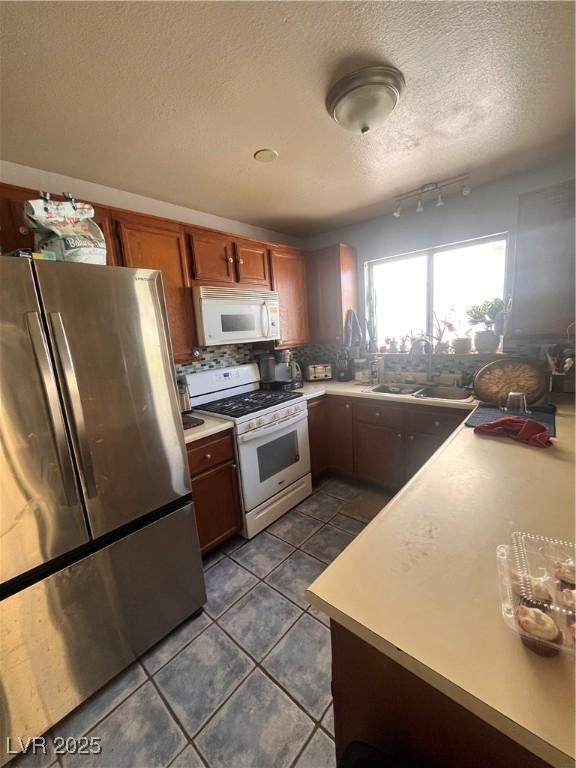 kitchen with a sink, white appliances, a textured ceiling, dark tile patterned flooring, and light countertops