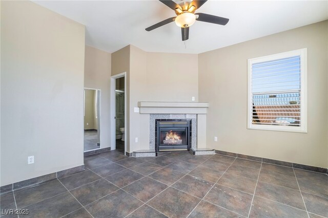 unfurnished living room with a ceiling fan, a lit fireplace, dark tile patterned floors, and baseboards