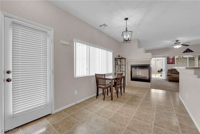 dining space featuring light tile patterned floors, baseboards, visible vents, ceiling fan with notable chandelier, and a fireplace