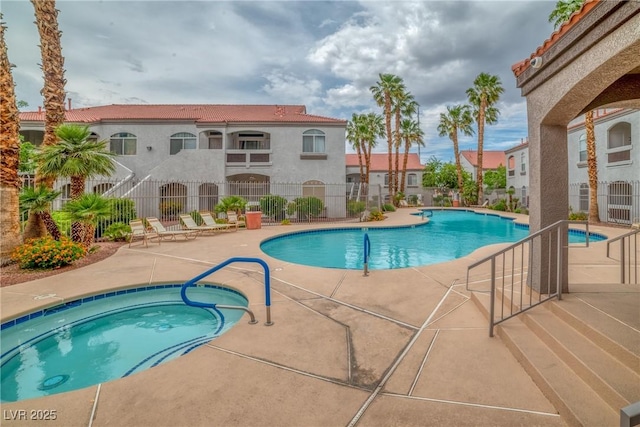 community pool with a hot tub, fence, and a patio