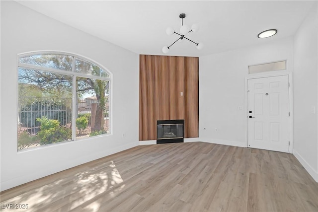 unfurnished living room featuring a chandelier, light wood-style floors, plenty of natural light, and a glass covered fireplace
