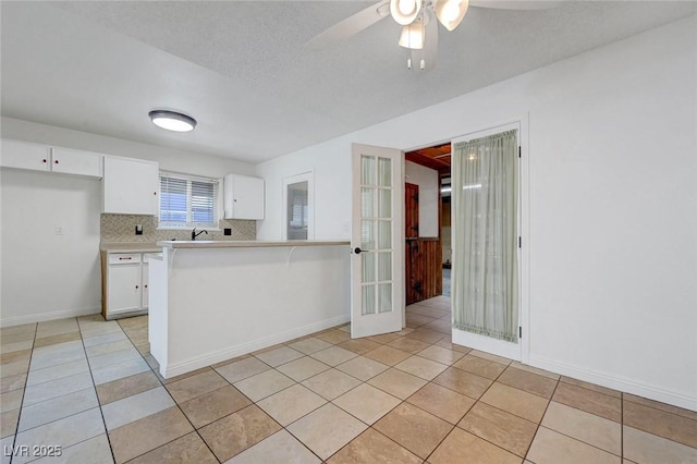 kitchen featuring light tile patterned floors, light countertops, a ceiling fan, white cabinetry, and baseboards