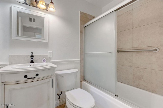 bathroom featuring toilet, a wainscoted wall, combined bath / shower with glass door, and vanity