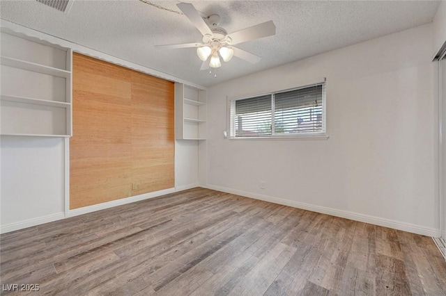 spare room featuring wood finished floors, baseboards, a textured ceiling, a ceiling fan, and built in features