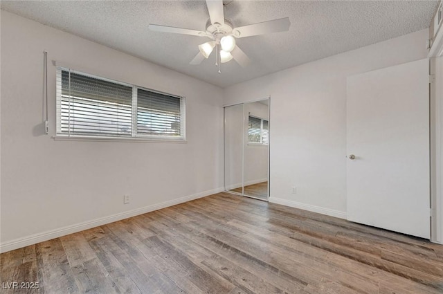 unfurnished bedroom with a textured ceiling, wood finished floors, baseboards, ceiling fan, and a closet