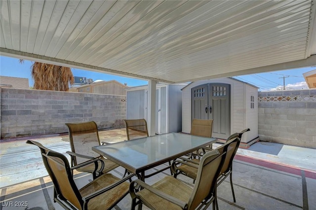 view of patio with a shed, outdoor dining area, a fenced backyard, and an outbuilding
