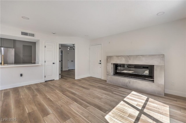 unfurnished living room with baseboards, a glass covered fireplace, visible vents, and wood finished floors