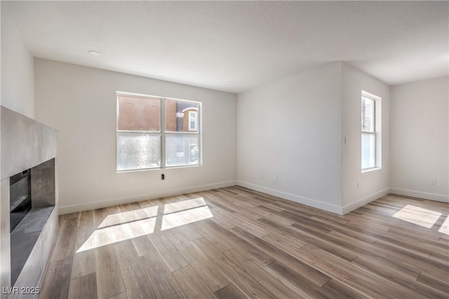 unfurnished living room featuring baseboards, a glass covered fireplace, and wood finished floors