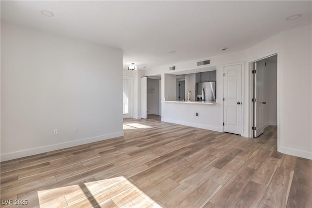 unfurnished living room featuring baseboards, light wood-style flooring, visible vents, and a sink