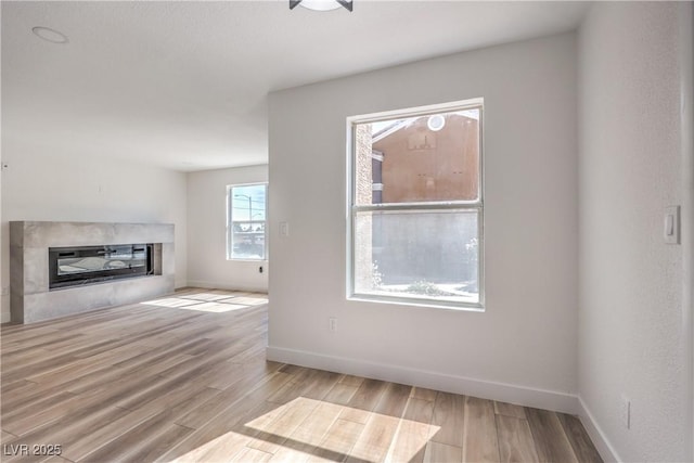 unfurnished living room with baseboards, a glass covered fireplace, and wood finished floors
