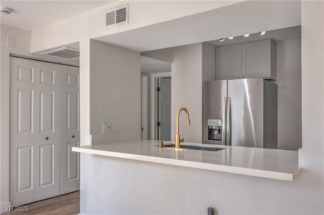 kitchen featuring visible vents, a sink, a peninsula, stainless steel refrigerator with ice dispenser, and wood finished floors
