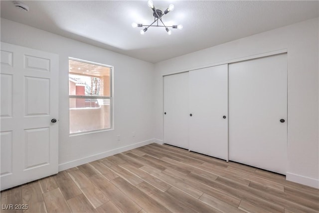 unfurnished bedroom with a closet, light wood-style floors, a chandelier, and baseboards