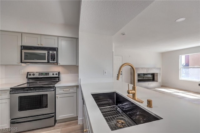 kitchen with a sink, light countertops, a premium fireplace, gray cabinetry, and appliances with stainless steel finishes