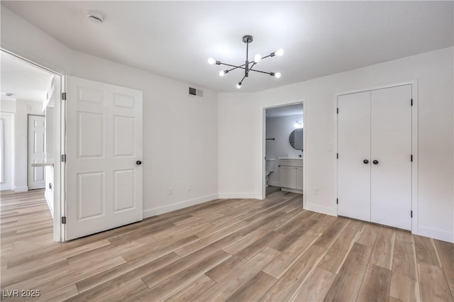 unfurnished bedroom featuring a notable chandelier, light wood-style flooring, baseboards, ensuite bathroom, and visible vents