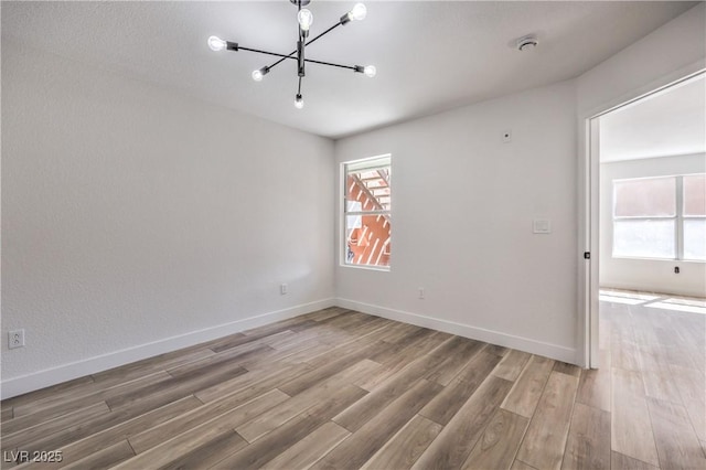 unfurnished room with light wood finished floors, baseboards, and a notable chandelier