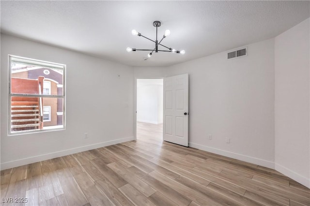 unfurnished room with light wood-type flooring, a notable chandelier, visible vents, and baseboards