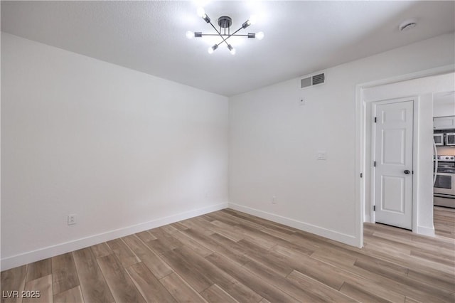 unfurnished room with baseboards, an inviting chandelier, light wood-style flooring, and visible vents