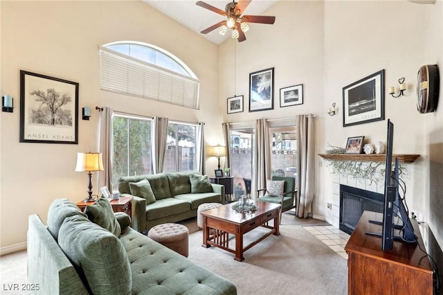 living room featuring high vaulted ceiling, a ceiling fan, light carpet, a tiled fireplace, and baseboards