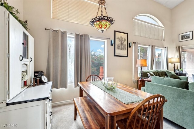 dining room featuring light colored carpet, a towering ceiling, and baseboards