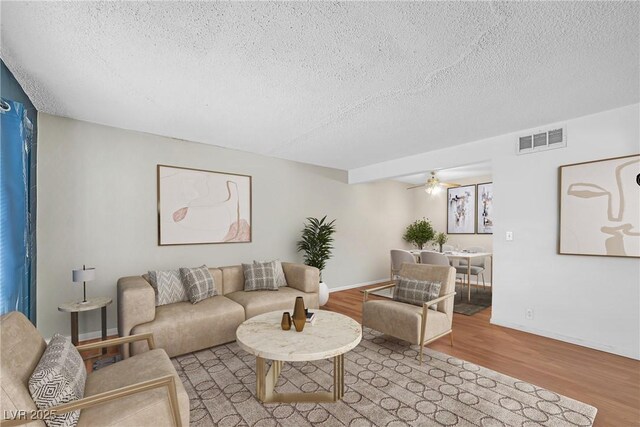 living room with a textured ceiling, wood finished floors, a ceiling fan, and baseboards