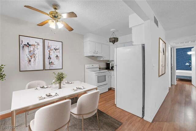 kitchen featuring white appliances, under cabinet range hood, light wood-style floors, white cabinetry, and a textured ceiling