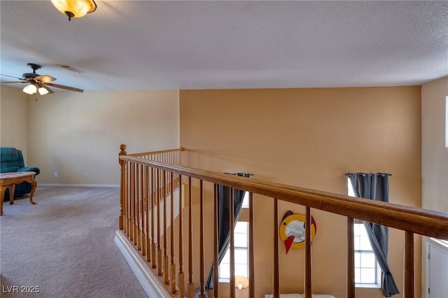 hallway featuring an upstairs landing, a textured ceiling, visible vents, baseboards, and light carpet