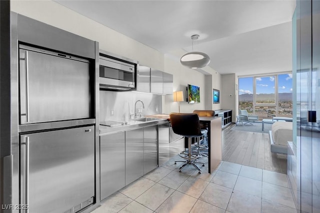 kitchen featuring modern cabinets, a sink, a wall of windows, light countertops, and appliances with stainless steel finishes