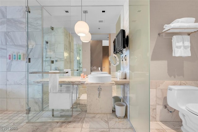 bathroom featuring toilet, a stall shower, a sink, tile walls, and marble finish floor