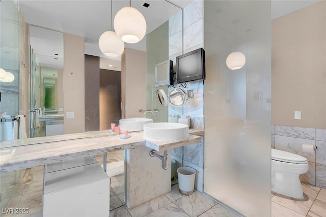 bathroom featuring tile walls, toilet, marble finish floor, visible vents, and a sink