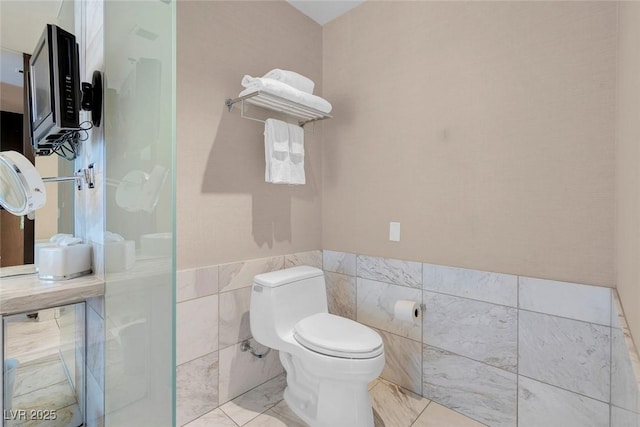 bathroom featuring a wainscoted wall, tile walls, and toilet