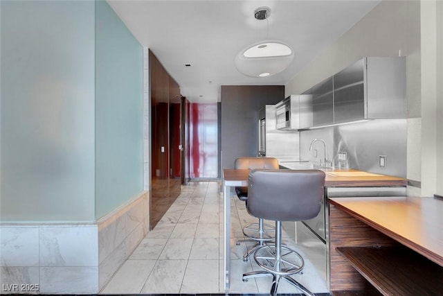 kitchen with stainless steel microwave, a sink, marble finish floor, pendant lighting, and light countertops