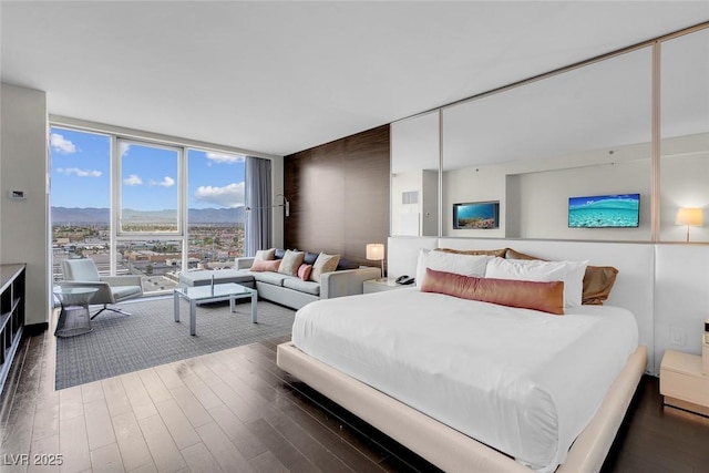 bedroom featuring a mountain view, expansive windows, and wood finished floors