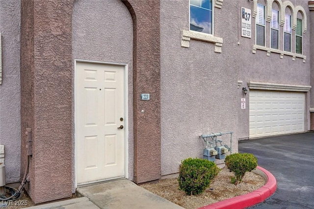property entrance with stucco siding, a garage, and aphalt driveway