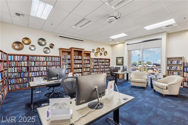 office area with a paneled ceiling, bookshelves, carpet flooring, and visible vents