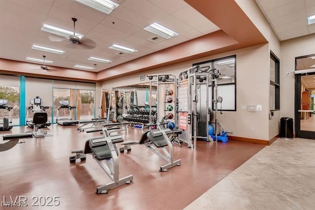 workout area with baseboards, a ceiling fan, a healthy amount of sunlight, and a paneled ceiling