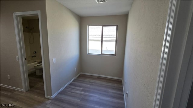 unfurnished bedroom featuring a textured wall, baseboards, visible vents, and wood finished floors