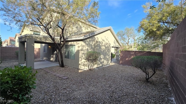 rear view of house with a gate, stucco siding, fence private yard, and a patio