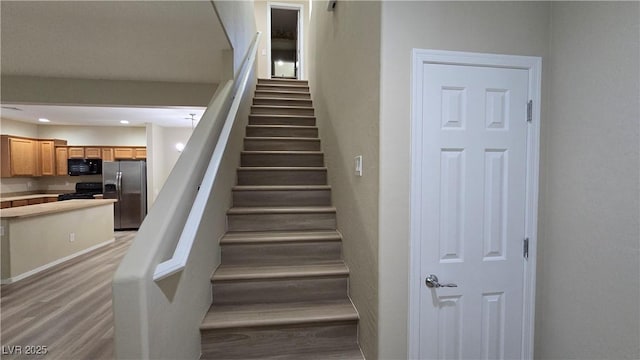 stairway with wood finished floors, baseboards, and recessed lighting