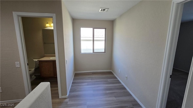 hallway with baseboards, visible vents, and wood finished floors